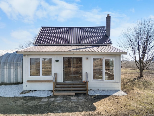 rear view of house with entry steps, metal roof, and a chimney