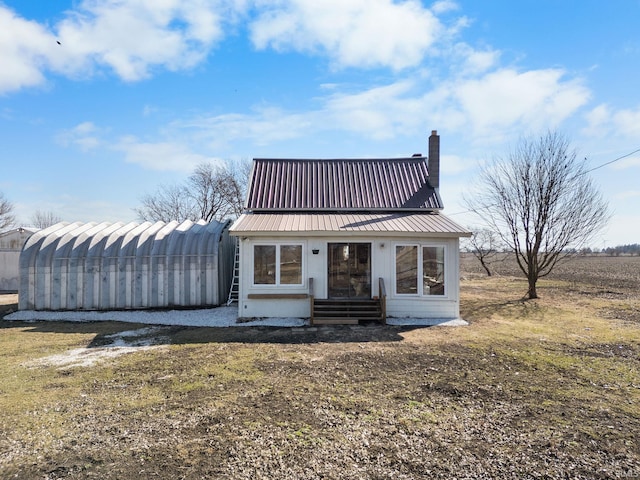 view of front of property featuring a chimney, entry steps, metal roof, and an outbuilding