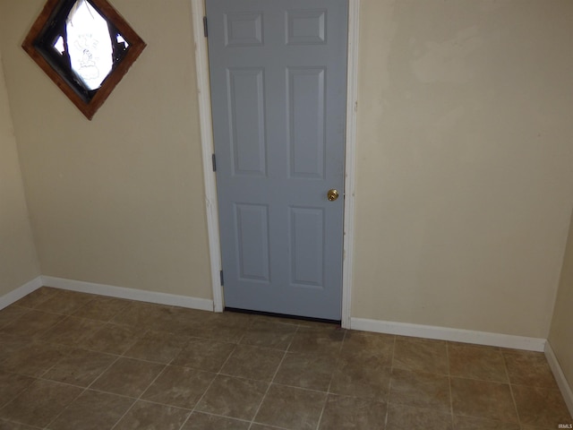 unfurnished room featuring dark tile patterned floors and baseboards