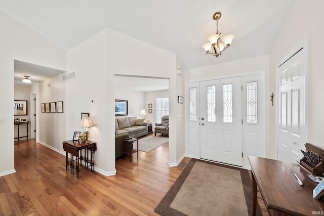 foyer featuring visible vents, a chandelier, wood finished floors, and vaulted ceiling