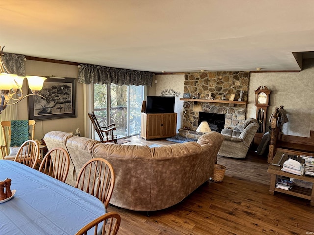 living room featuring a stone fireplace, a notable chandelier, wood finished floors, and ornamental molding