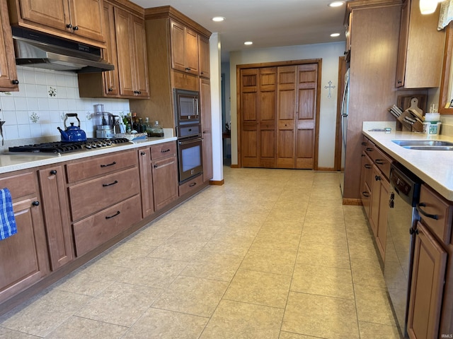 kitchen featuring under cabinet range hood, a sink, tasteful backsplash, appliances with stainless steel finishes, and light countertops