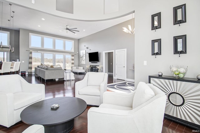 living room featuring dark wood-type flooring, baseboards, recessed lighting, ceiling fan with notable chandelier, and a high ceiling