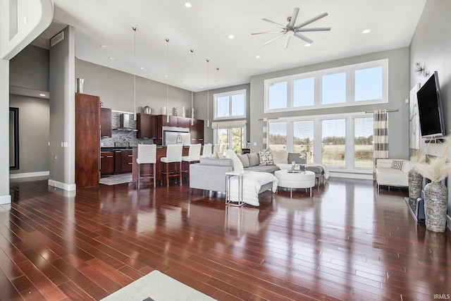 living area with recessed lighting, baseboards, a high ceiling, and dark wood-style floors