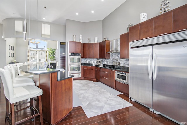 kitchen featuring dark countertops, backsplash, appliances with stainless steel finishes, a towering ceiling, and a sink