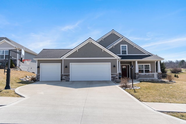 craftsman house with a front yard, driveway, covered porch, and stone siding