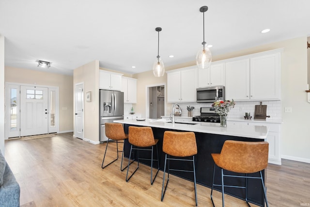 kitchen featuring light wood-style flooring, an island with sink, stainless steel appliances, light countertops, and tasteful backsplash