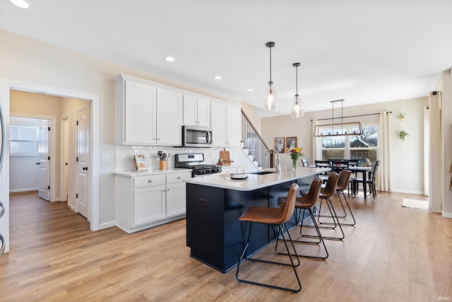 kitchen featuring tasteful backsplash, light countertops, light wood-style flooring, stainless steel appliances, and white cabinetry