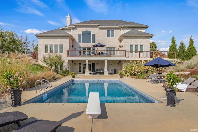 rear view of property featuring a patio, a balcony, outdoor dining area, an outdoor pool, and a chimney