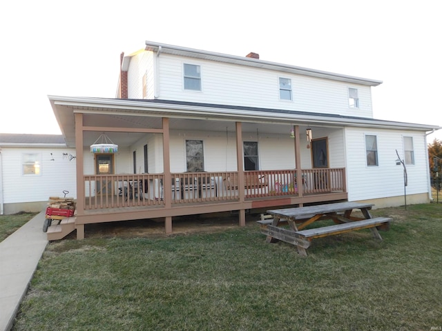 rear view of house with covered porch, a chimney, and a yard