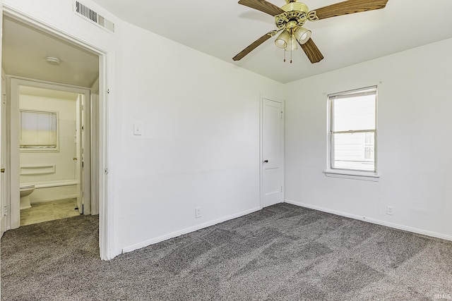 unfurnished bedroom with visible vents, a ceiling fan, ensuite bathroom, dark colored carpet, and baseboards