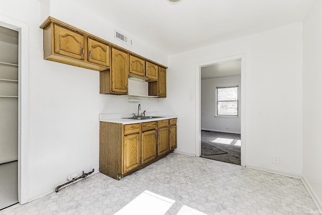 kitchen featuring a sink, visible vents, brown cabinetry, and light countertops