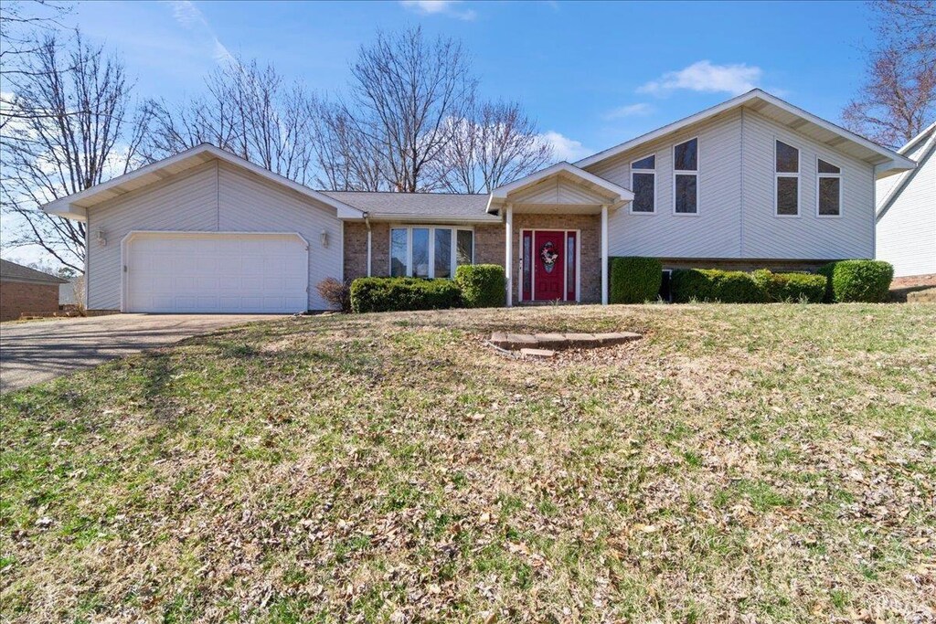 tri-level home featuring a garage, a front yard, brick siding, and driveway