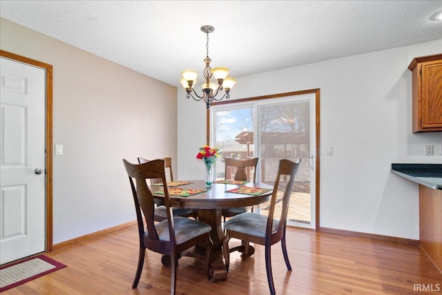 dining space with an inviting chandelier, baseboards, light wood-type flooring, and a textured ceiling