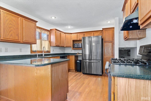 kitchen featuring range hood, a peninsula, a sink, stainless steel appliances, and dark countertops