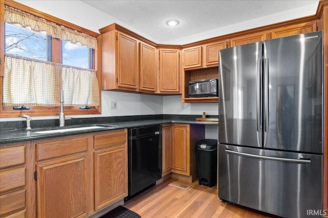 kitchen with brown cabinetry, light wood-style flooring, a sink, black appliances, and a textured ceiling