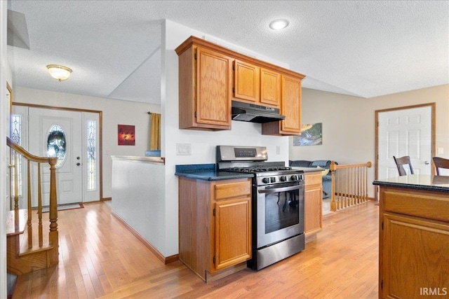 kitchen featuring under cabinet range hood, dark countertops, gas stove, and light wood-type flooring