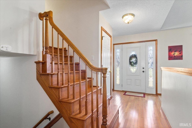 entrance foyer with a textured ceiling, stairs, baseboards, and wood-type flooring