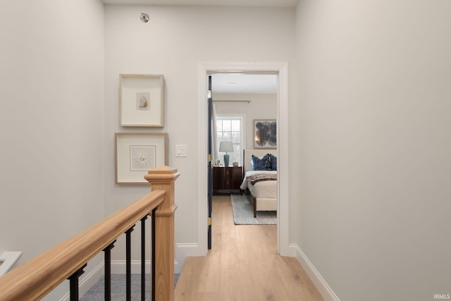 corridor featuring baseboards, an upstairs landing, and light wood-style floors