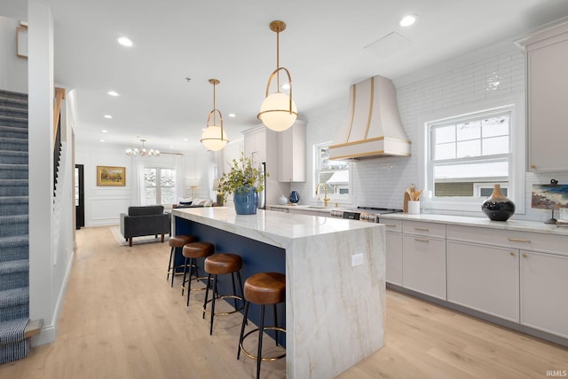 kitchen featuring a kitchen island, premium range hood, light wood finished floors, and a sink