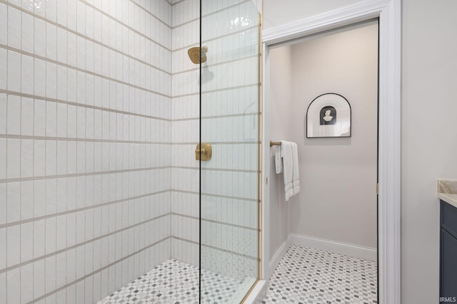 bathroom with a tile shower, vanity, and baseboards