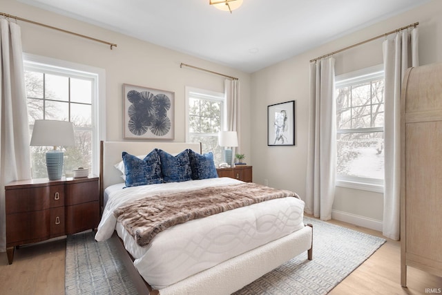 bedroom with multiple windows, light wood-style floors, and baseboards