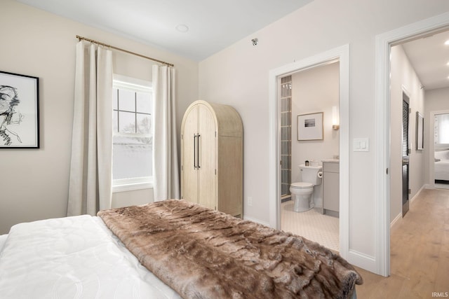 bedroom with baseboards, multiple windows, light wood-style floors, and ensuite bathroom