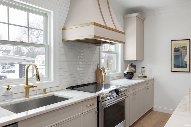 kitchen with backsplash, a healthy amount of sunlight, stainless steel electric range oven, custom exhaust hood, and a sink