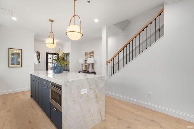 kitchen featuring baseboards, light wood-style flooring, ornamental molding, stainless steel microwave, and a center island