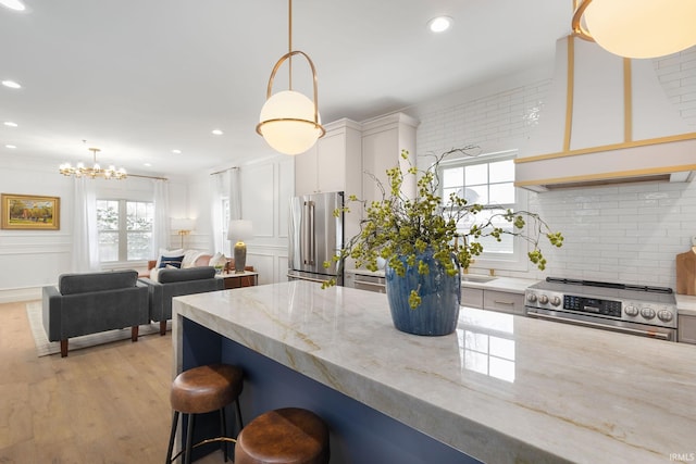 kitchen featuring a breakfast bar area, light stone countertops, light wood-style floors, appliances with stainless steel finishes, and tasteful backsplash