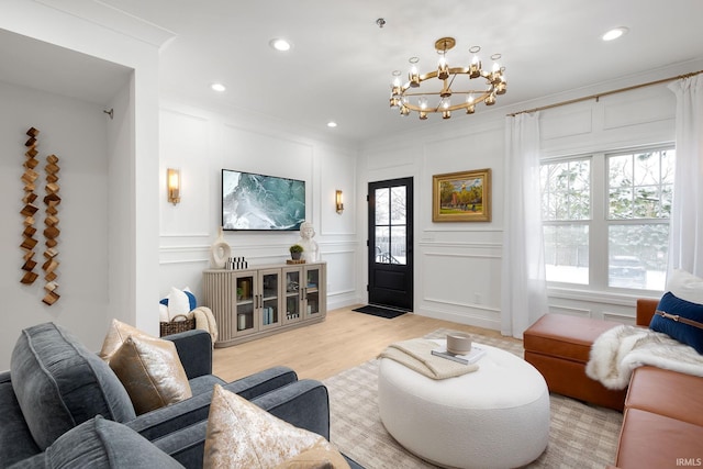 living room with an inviting chandelier, crown molding, a decorative wall, and light wood-style floors