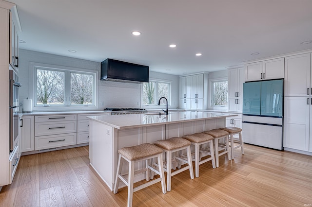 kitchen with light wood finished floors, a sink, light countertops, white cabinets, and wall chimney exhaust hood