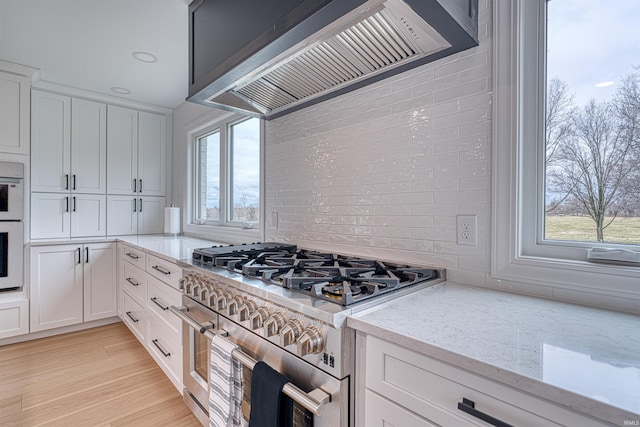 kitchen featuring premium range hood, tasteful backsplash, white cabinetry, range with two ovens, and light stone countertops