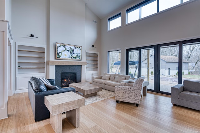 living area with built in shelves, a fireplace, light wood finished floors, and a healthy amount of sunlight