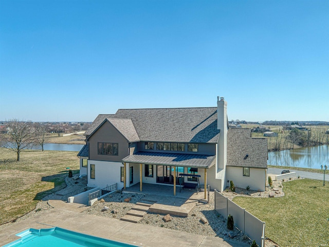 rear view of house with a patio, a standing seam roof, a yard, a water view, and metal roof