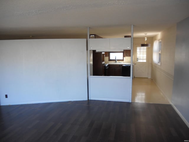 unfurnished living room featuring a sink, a textured ceiling, baseboards, and wood finished floors