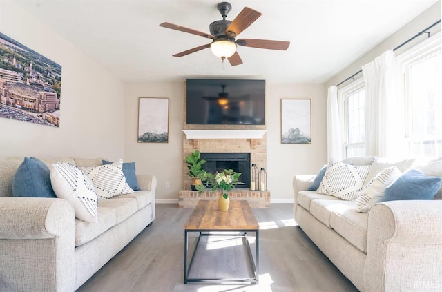 living area featuring ceiling fan, a fireplace, baseboards, and wood finished floors