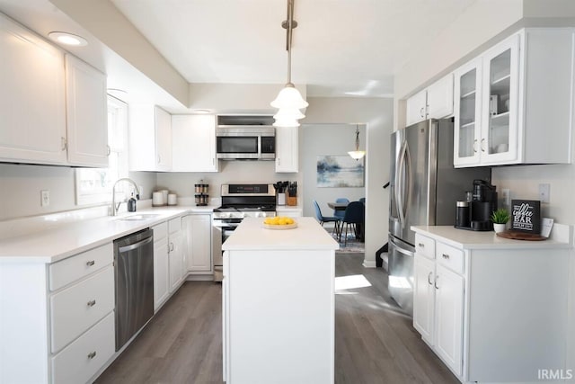 kitchen with a sink, glass insert cabinets, appliances with stainless steel finishes, white cabinetry, and a center island