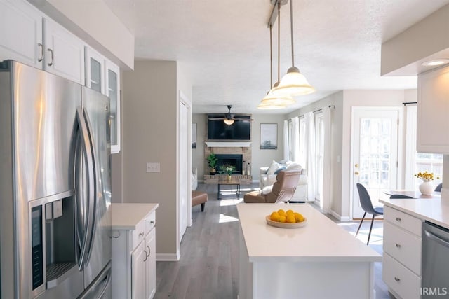 kitchen featuring a fireplace with raised hearth, a center island, light countertops, appliances with stainless steel finishes, and white cabinets