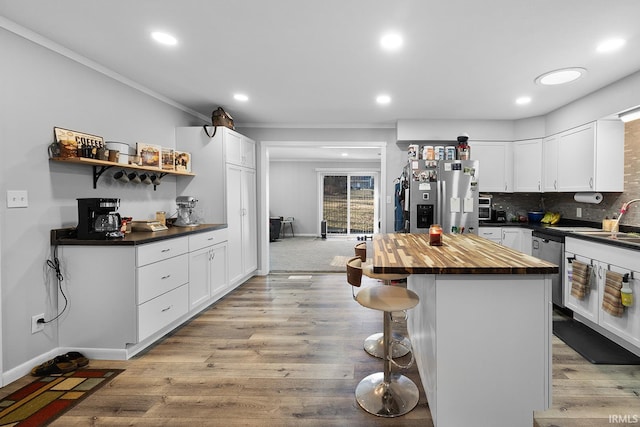 kitchen with butcher block countertops, white cabinets, a kitchen breakfast bar, and stainless steel appliances