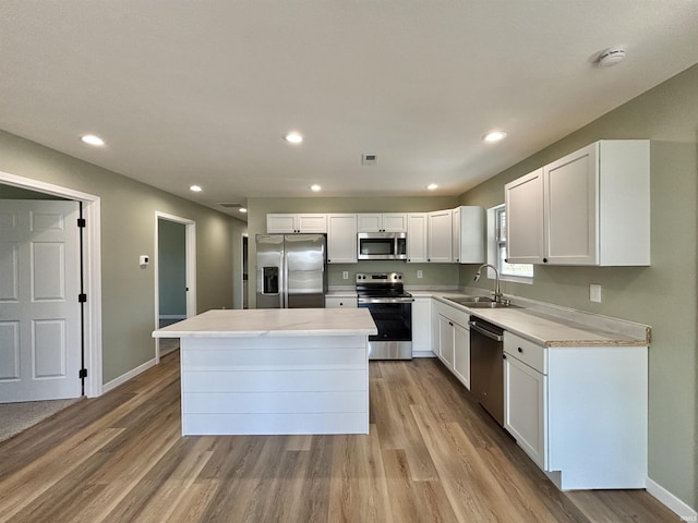 kitchen with a kitchen island, a sink, white cabinets, appliances with stainless steel finishes, and light wood-type flooring