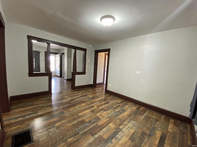 empty room with visible vents, dark wood-type flooring, and baseboards