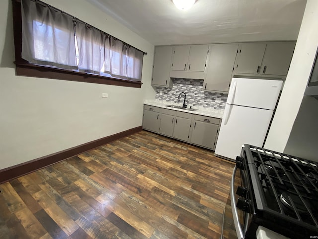 kitchen featuring dark wood-style floors, freestanding refrigerator, gray cabinetry, a sink, and gas range