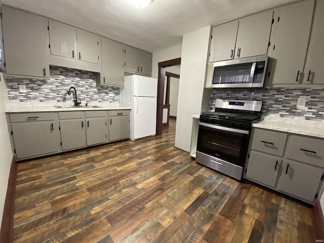 kitchen with gray cabinets, a sink, backsplash, dark wood-style floors, and stainless steel appliances