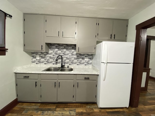 kitchen with dark wood-style flooring, gray cabinets, freestanding refrigerator, a sink, and tasteful backsplash