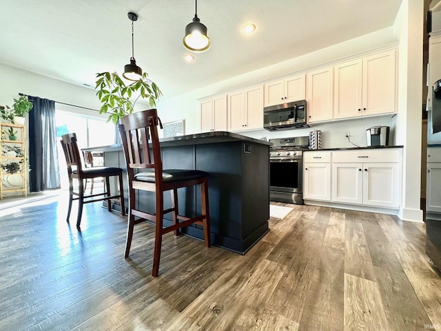 kitchen with dark countertops, appliances with stainless steel finishes, white cabinetry, and wood finished floors