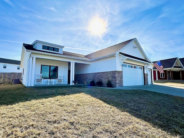 view of front of house featuring a front lawn, stone siding, a porch, fence, and a garage