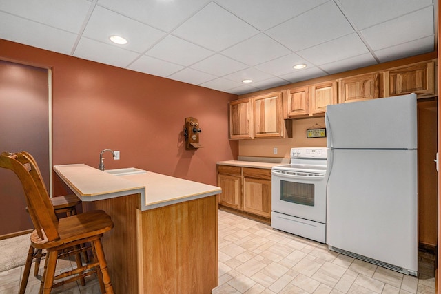 kitchen with white appliances, a sink, light countertops, a paneled ceiling, and a kitchen bar