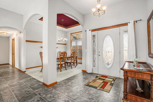 foyer entrance featuring carpet flooring, arched walkways, baseboards, and a chandelier