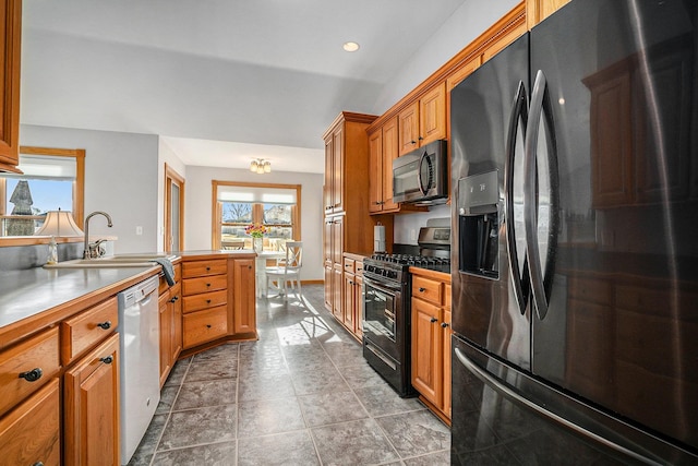 kitchen with recessed lighting, a peninsula, brown cabinetry, black appliances, and a sink